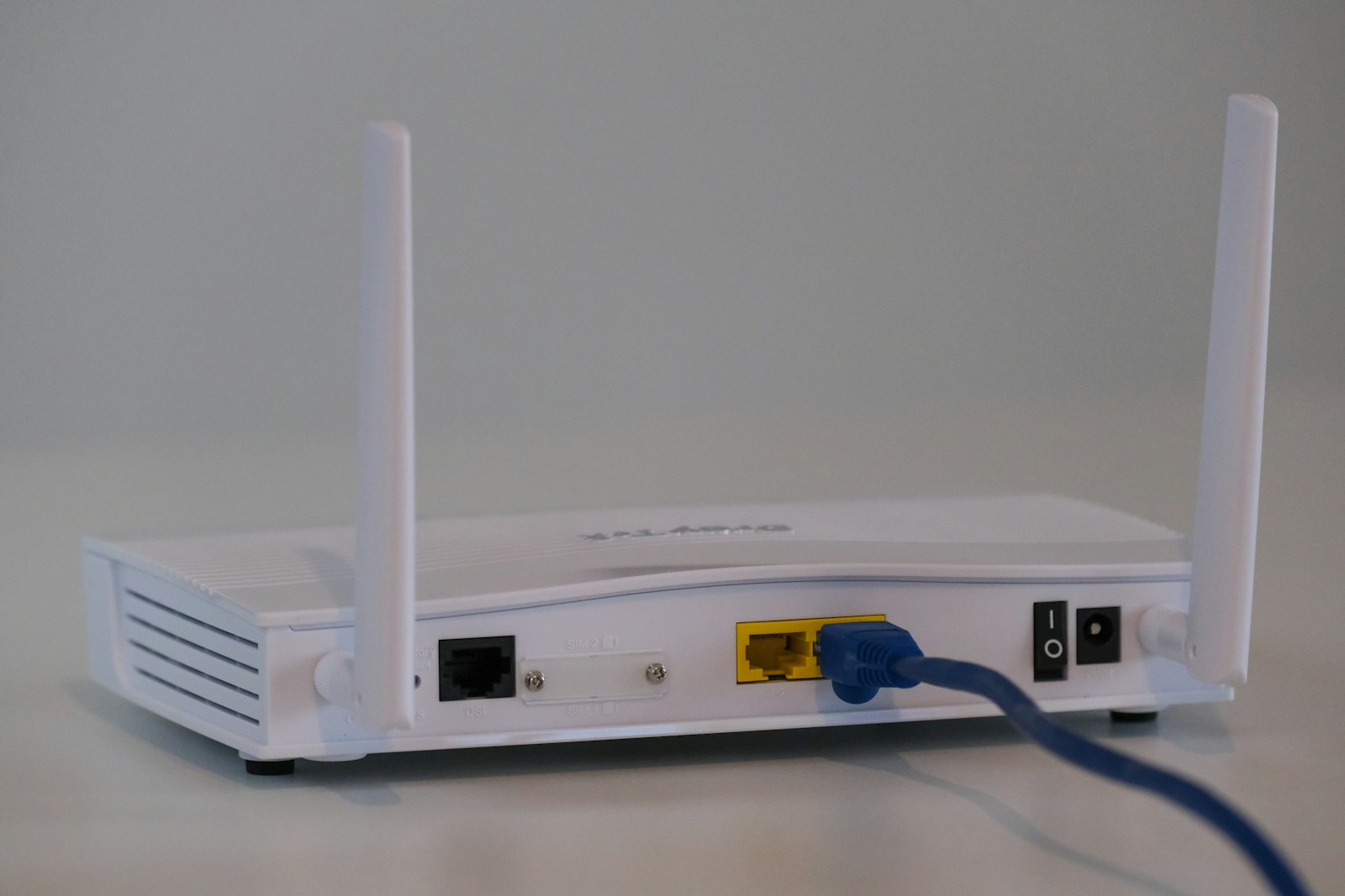 A wireless router with antennas on a desk, with a laptop open nearby